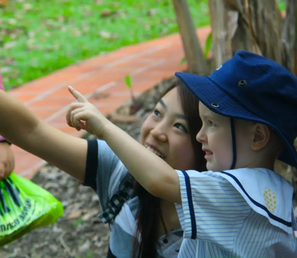 幼儿园的孩子在成人身旁指向户外的某样东西。