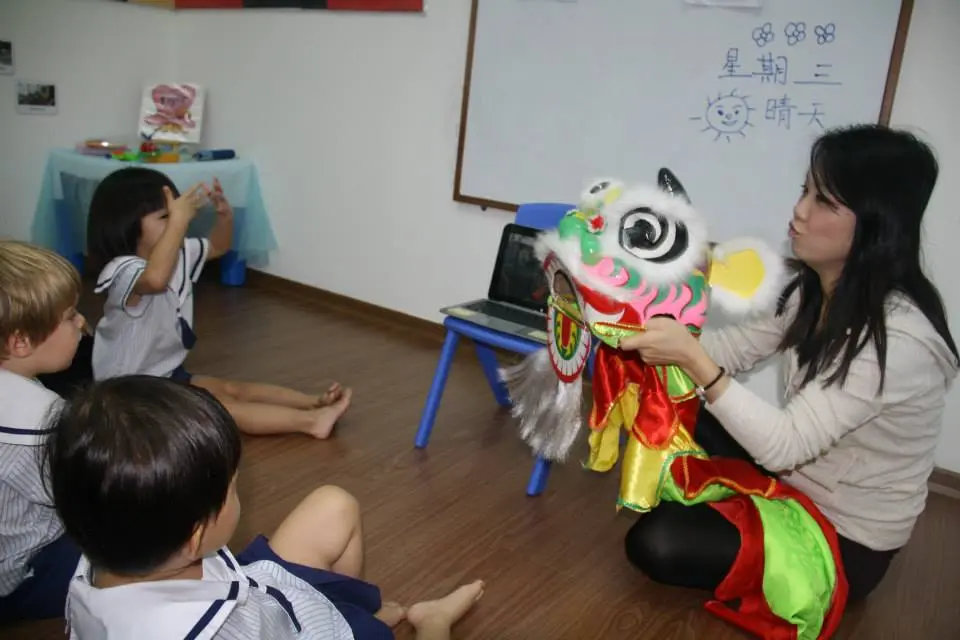 老师向坐着的学龄前儿童展示舞狮狮头。