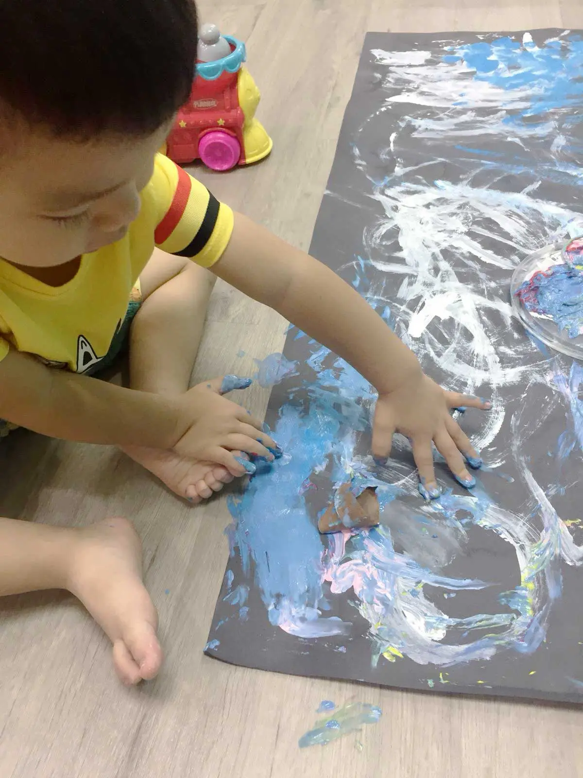 暗い色の紙に両手で青と白の絵の具を広げる子ども。