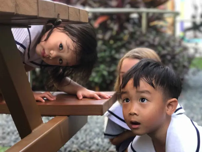 屋外でテーブルの下を探索し遊ぶ子どもたち